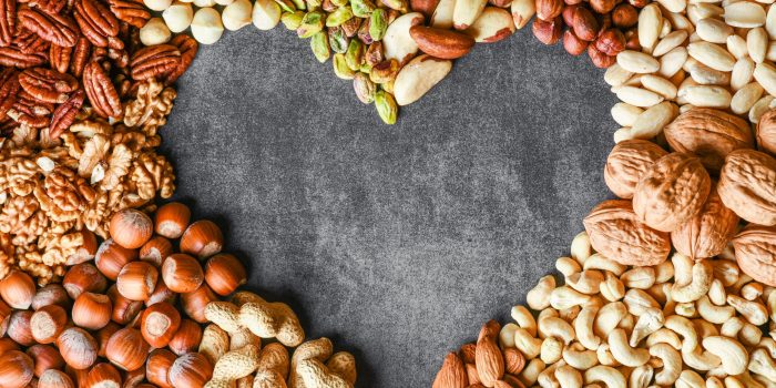 Natural healthy background made from different kinds of mixed nuts like walnuts, hazelnut, pistachio, almond, cashew, pecans. Heart shape top view.
